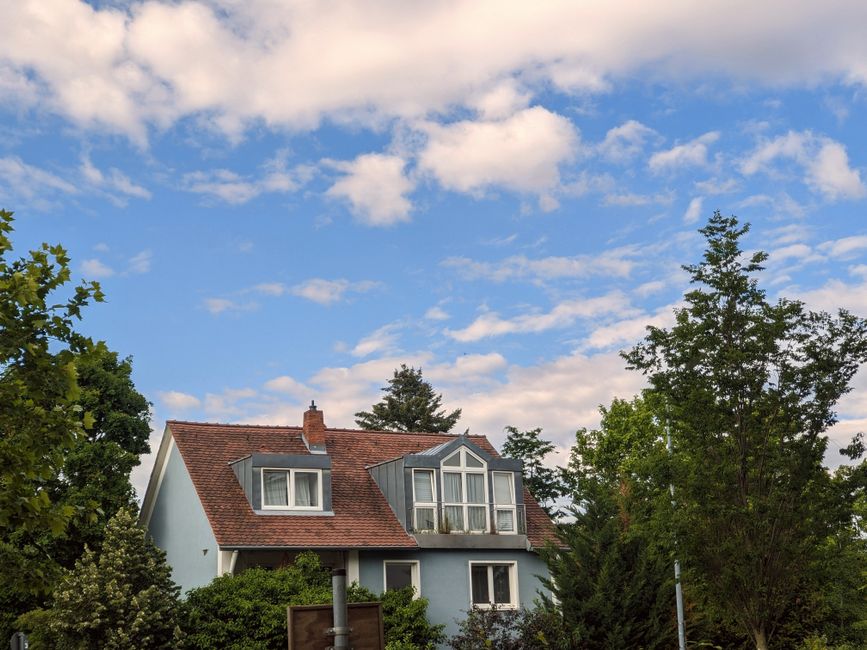 Vue pittoresque d'une maison classique avec un toit rouge sur fond de ciel bleu vif, entourée de verdure.